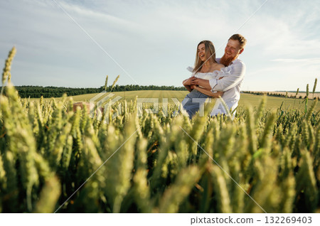 Man is embracing his woman. Lovely couple are on the green agricultural field together Man is embracing his woman. Lovely couple are on the green agricultural field together 132269403