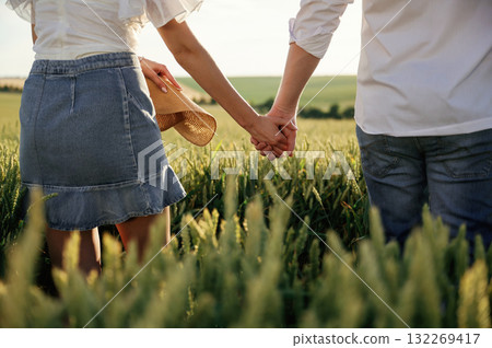 Close up view, holding each other's hands. Lovely couple are on the green agricultural field together 132269417
