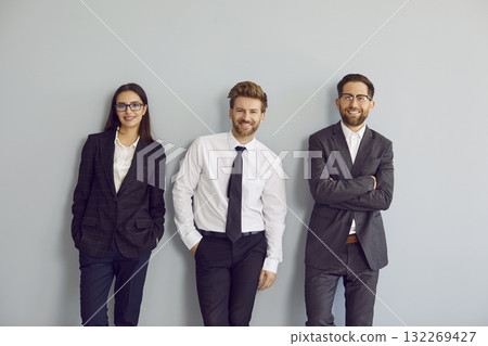 Team of happy young business people wearing formal office clothes standing by wall Team of happy young business people wearing formal office clothes standing by wall 132269427