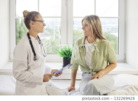 Smiling patient talking with female doctor during healthcare appointment in clinic 132269428