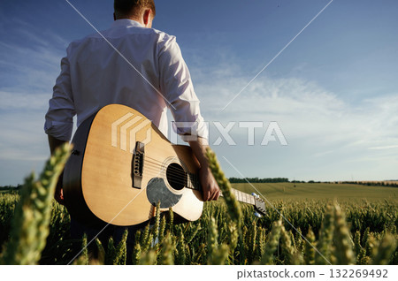 Musician is with acoustic guitar. Man in white shirt is on the agricultural field Musician is with acoustic guitar. Man in white shirt is on the agricultural field 132269492