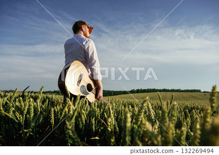 Musician is with acoustic guitar. Man in white shirt is on the agricultural field 132269494