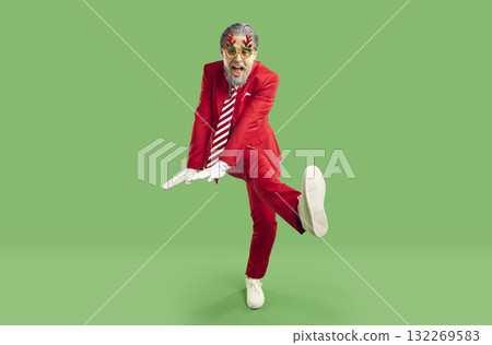 Crazy funny senior bearded grey haired man in glasses with deer antlers dancing on green background. Crazy funny senior bearded grey haired man in glasses with deer antlers dancing on green background. 132269583