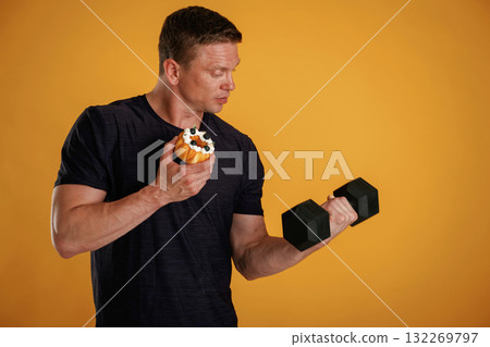 Dumbbell or cake, choice. Man is against background in the studio 132269797