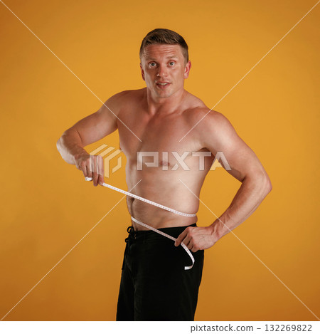Measuring the waist, muscular guy. Man is against background in the studio 132269822