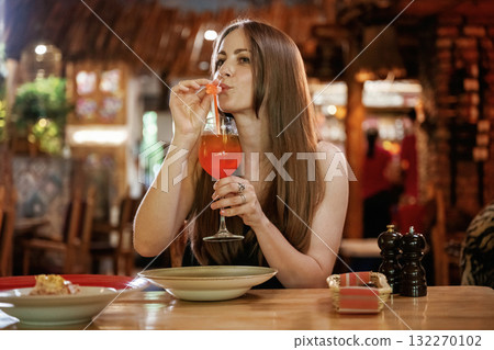 Red cocktail, drinking. Woman is in the restaurant with food and drink 132270102