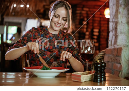 Uses a fork and a knife. Woman is in the restaurant with food and drink Uses a fork and a knife. Woman is in the restaurant with food and drink 132270137