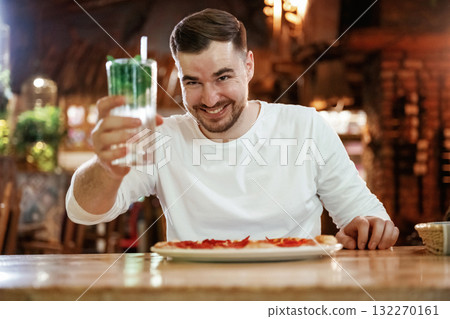 With mojito. Man is sitting in the restaurant and eating a pizza With mojito. Man is sitting in the restaurant and eating a pizza 132270161