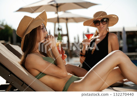 Straw hats and sunglasses, with drinks. Two beautiful women are resting near the pool 132270440