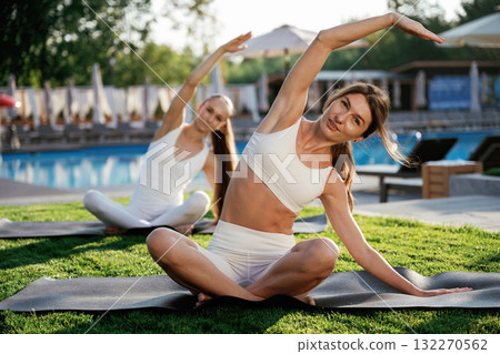 On the yoga mats, doing exercises. Two fitness women are together outdoors, conception of sport On the yoga mats, doing exercises. Two fitness women are together outdoors, conception of sport 132270562