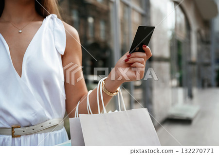 Credit card is in hand. Stylish woman is with shopping bag outdoors near the building Credit card is in hand. Stylish woman is with shopping bag outdoors near the building 132270771