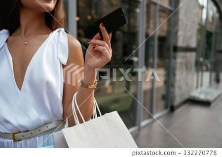 Black credit card in hand. Stylish woman is with shopping bag outdoors near the building 132270778