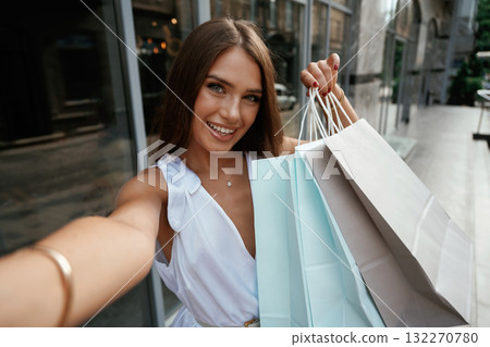 Making a selfie, smiling. Stylish woman is with shopping bag outdoors near the building 132270780