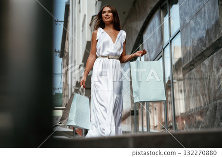 Taking a walk. Stylish woman is with shopping bag outdoors near the building Taking a walk. Stylish woman is with shopping bag outdoors near the building 132270880