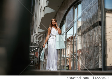 Talking by a phone. Stylish woman is with shopping bag outdoors near the building 132270892