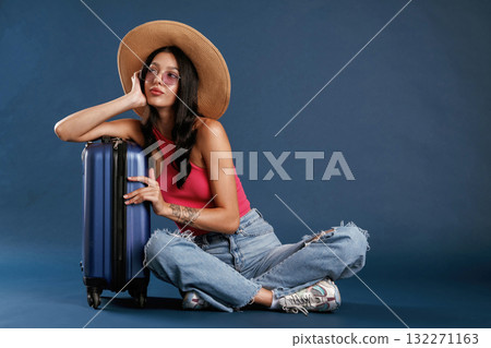 Taking a rest, sitting with suitcase. Beautiful young woman is against background 132271163