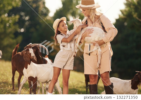 Holding animal in hands. Mother and daughter are together on the farm with goats Holding animal in hands. Mother and daughter are together on the farm with goats 132271350