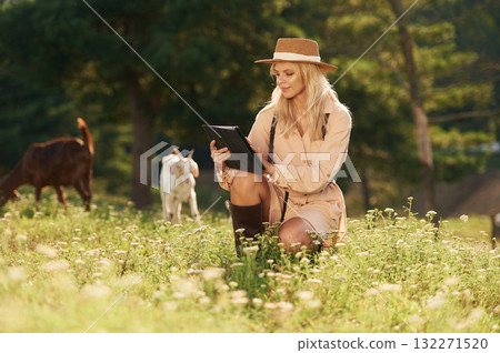 With black digital tablet. Young woman is on the field, farm, with the goats With black digital tablet. Young woman is on the field, farm, with the goats 132271520