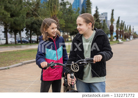 Happy child girls 10 and 12 years old with bicycle walking outdoors 132271772