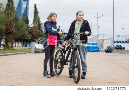 Cheerful young girls talking and walking together. Children with bikes outdoors 132271773