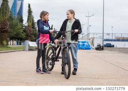 Full length portrait of young girls talking and walking together. Children with bikes outdoors 132271779