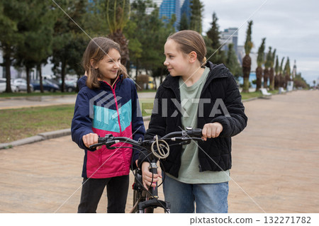 Cheerful children girls 10 and 12 years old with bicycle walking outdoors Cheerful children girls 10 and 12 years old with bicycle walking outdoors 132271782