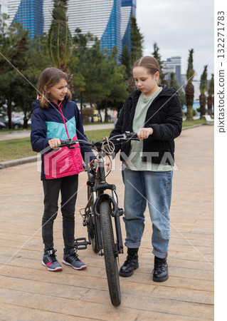 Serious young girls talking and walking together. Children with bikes outdoors Serious young girls talking and walking together. Children with bikes outdoors 132271783