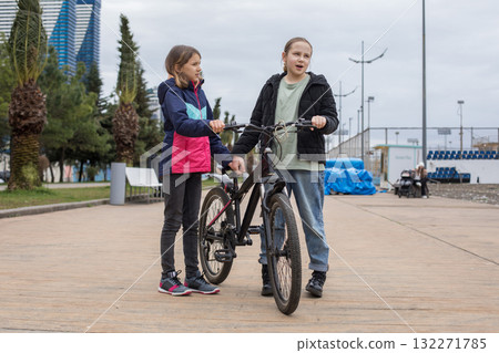Adorable young girls talking and walking together. Children with bikes outdoors Adorable young girls talking and walking together. Children with bikes outdoors 132271785