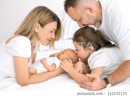 The older sister gently kisses her newborn brother. A baby surrounded by loving parents. The older sister gently kisses her newborn brother. A baby surrounded by loving parents. 132272135