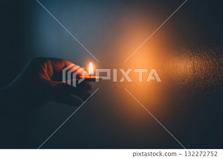 Single hand holding lit candle in quiet, dimly lit room creates warm, peaceful atmosphere with soft shadows on smooth wall, evoking calm and solitude Single hand holding lit candle in quiet, dimly lit room creates warm, peaceful atmosphere with soft shadows on smooth wall, evoking calm and solitude 132272752