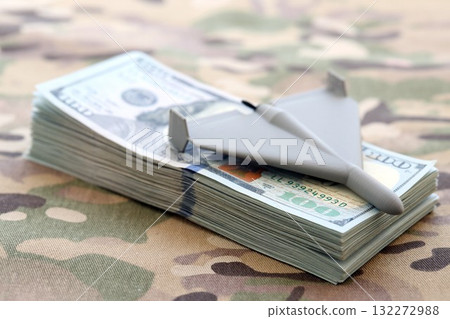 Unnamed grey toy drone and dollar bills on camouflage fabric close up. Drone manufacturing funds Unnamed grey toy drone and dollar bills on camouflage fabric close up. Drone manufacturing funds 132272988