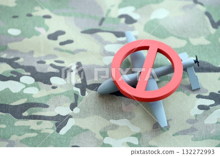 Unnamed grey toy drone model and red prohibition sign on camouflage fabric close up. Anti-aircraft warfare concept Unnamed grey toy drone model and red prohibition sign on camouflage fabric close up. Anti-aircraft warfare concept 132272993