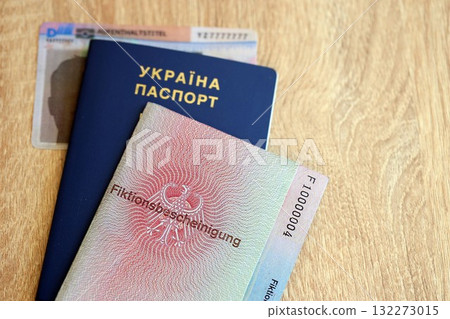 German Permanent resident card and document specimen lies with Ukrainian passport on wooden table close up. Aufenthaltstitel and Fiktionsbescheinigung German Permanent resident card and document specimen lies with Ukrainian passport on wooden table close up. Aufenthaltstitel and Fiktionsbescheinigung 132273015