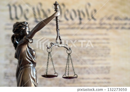 Lady Justice bronze statue with scales on background of US Constitution page close up. Lawsuit and punishment in United States 132273050