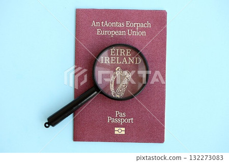 Ireland passport and magnifying glass on light blue paper background close up. Citizenship details and information concept Ireland passport and magnifying glass on light blue paper background close up. Citizenship details and information concept 132273083