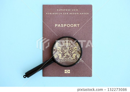 Netherlands passport and magnifying glass on light blue paper background close up. Citizenship details and information concept Netherlands passport and magnifying glass on light blue paper background close up. Citizenship details and information concept 132273086