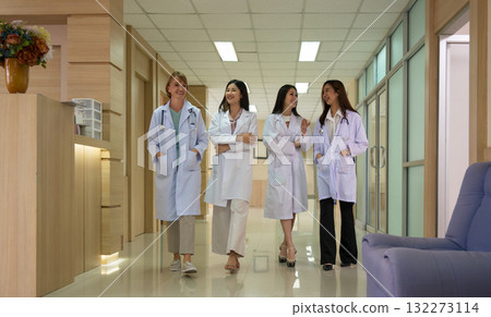 Four female healthcare professionals in white lab coats walking together down modern hospital corridor while smiling and appearing friendly Four female healthcare professionals in white lab coats walking together down modern hospital corridor while smiling and appearing friendly 132273114