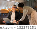 Smiling businessman working on laptop aboard airplane while friendly woman flight attendant provides service 132273151