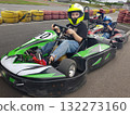 A cute child wearing a yellow helmet enjoying a thrilling ride on a karting track  132273160