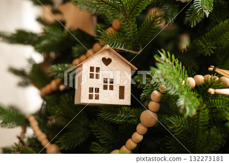 A charming wooden miniature house ornament hangs on a Christmas tree 132273181
