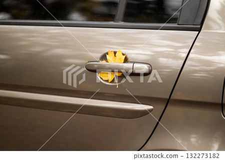 Yellow autumn leaf stuck in a car door handle, symbolizing fall season and nature meeting urban life. Yellow autumn leaf stuck in a car door handle, symbolizing fall season and nature meeting urban life. 132273182