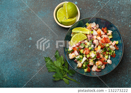 Peruvian seafood ceviche with shrimps, octopus, tomatoes, cucumber, and parsley in a bowl served with lime top view, space for text 132273222