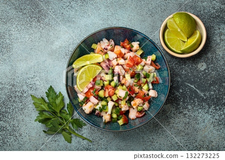 Peruvian seafood ceviche with shrimps, octopus, tomatoes, cucumber, and parsley in a bowl served with lime top view Peruvian seafood ceviche with shrimps, octopus, tomatoes, cucumber, and parsley in a bowl served with lime top view 132273225