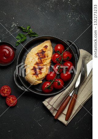 Grilled chicken breast fillet with cherry tomatoes in cast iron pan and tomato sauce top view on rustic black background, healthy food 132273233