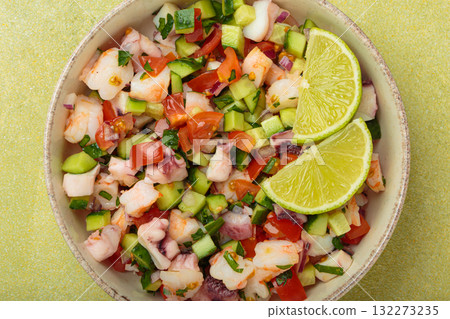 Peruvian seafood ceviche with shrimps, octopus, tomatoes, cucumber, and parsley in a bowl served with lime top view Peruvian seafood ceviche with shrimps, octopus, tomatoes, cucumber, and parsley in a bowl served with lime top view 132273235