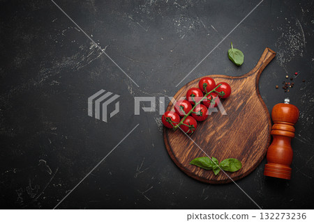 Food background with fresh vegetables, cooking ingredients, spices resting on rustic wooden cutting board, black background, space for text 132273236