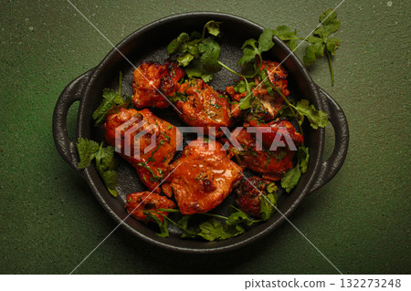 Delicious tandoori chicken garnished with coriander in cast iron pan top view on green background Delicious tandoori chicken garnished with coriander in cast iron pan top view on green background 132273248