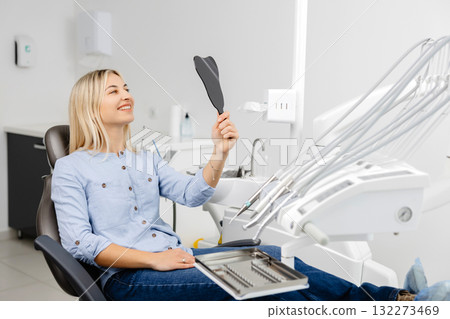Patient admiring smile after dental checkup using small mirror in modern clinic 132273469