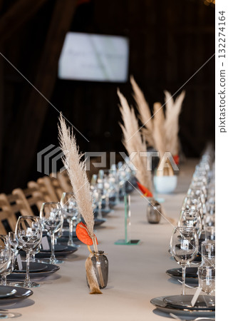 Rustic Wedding Table Setting with Pampas Grass Centerpieces, Gray Plates, and Glassware in a Dark Barn Interior, Warm Toned Photography. 132274164