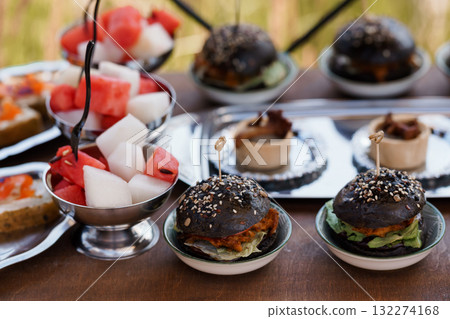 Gourmet Black Burger Bites with Watermelon Skewers on Silver Platters, Outdoor Catering, Rustic Style Food Photography, Vibrant Colors. Gourmet Black Burger Bites with Watermelon Skewers on Silver Platters, Outdoor Catering, Rustic Style Food Photography, Vibrant Colors. 132274168